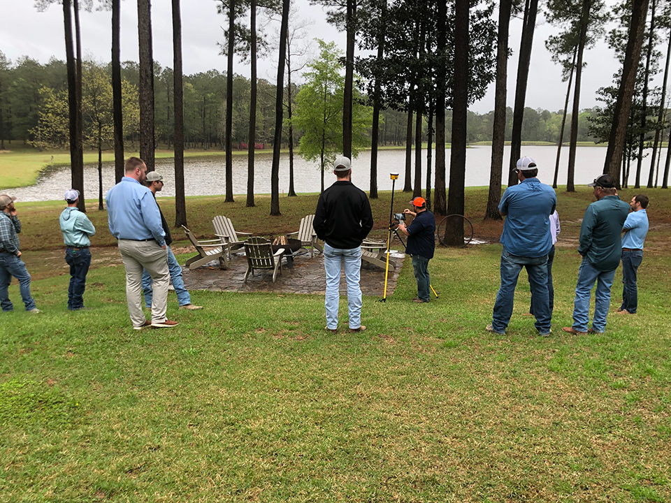 SITECH Louisiana team members watching a construction technology demonstration outdoors.